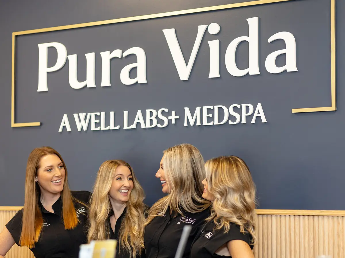 The Pura Vida team smiling in front of the Pura Vida, A Well Labs+ Medspa sign at the Fleming Island, FL studio