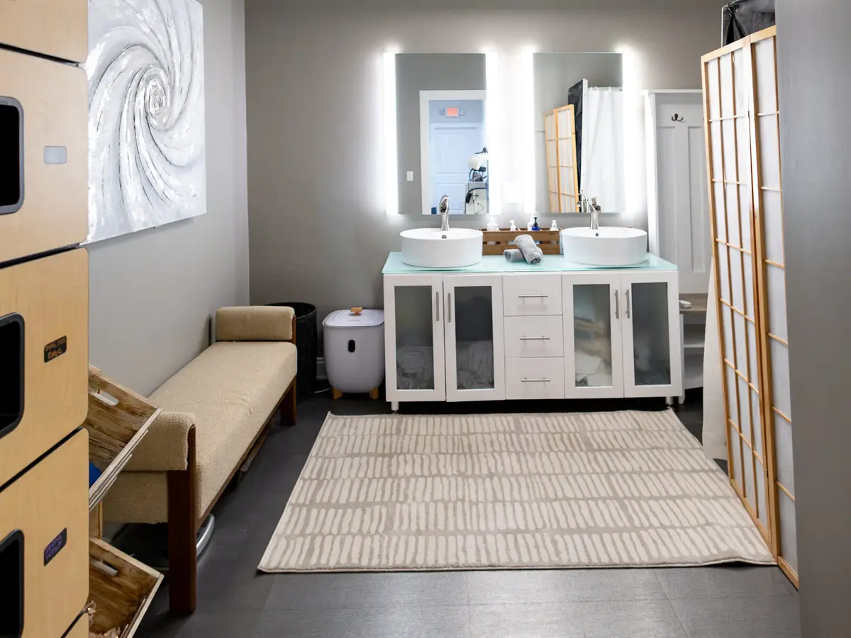 The Pura Vida guest locker room with a lit double vanity and cushioned bench in Fleming Island, FL