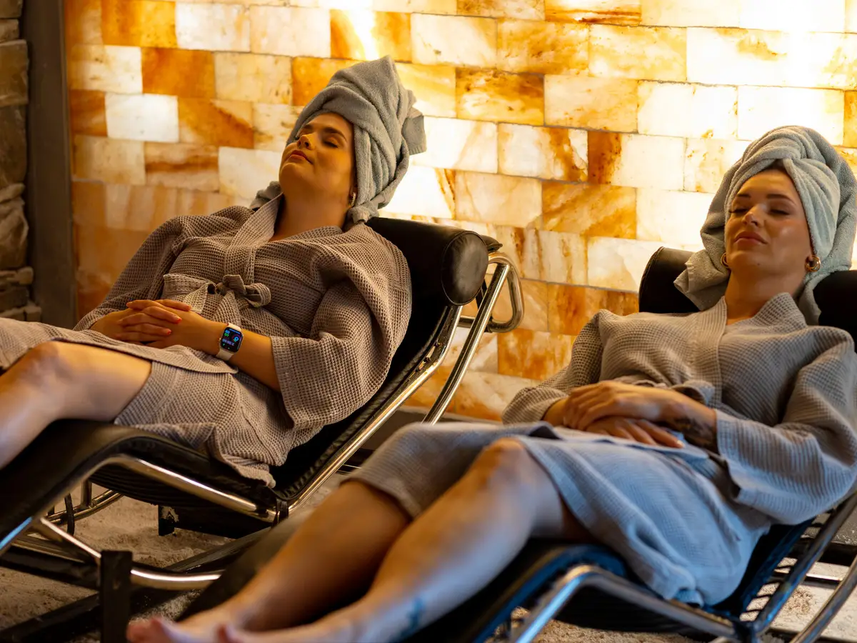 Two Pura Vida guests in robes relaxing on loungers beside a glowing Himalayan salt wall in Fleming Island, FL